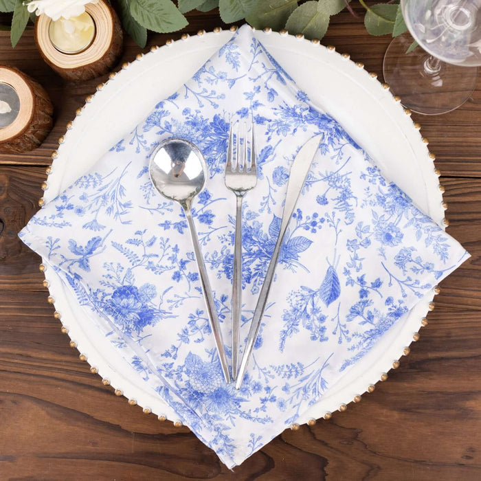 Silver cutlery on a blue floral napkin atop a decorative plate.