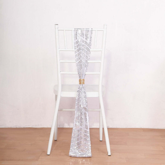 Silver sequin chair sash tied on a white chair against a plain backdrop.