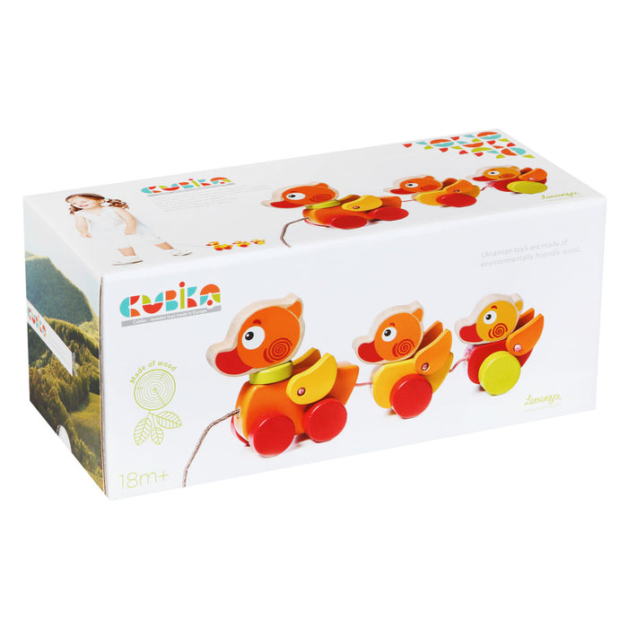 The box packaging shows Cubika Wooden Walk-A-Long Traveling Ducks—an organic wooden pull toy with three colorful ducklings on wheels, suitable for children 18 months+, and displays a child playing with the toy.