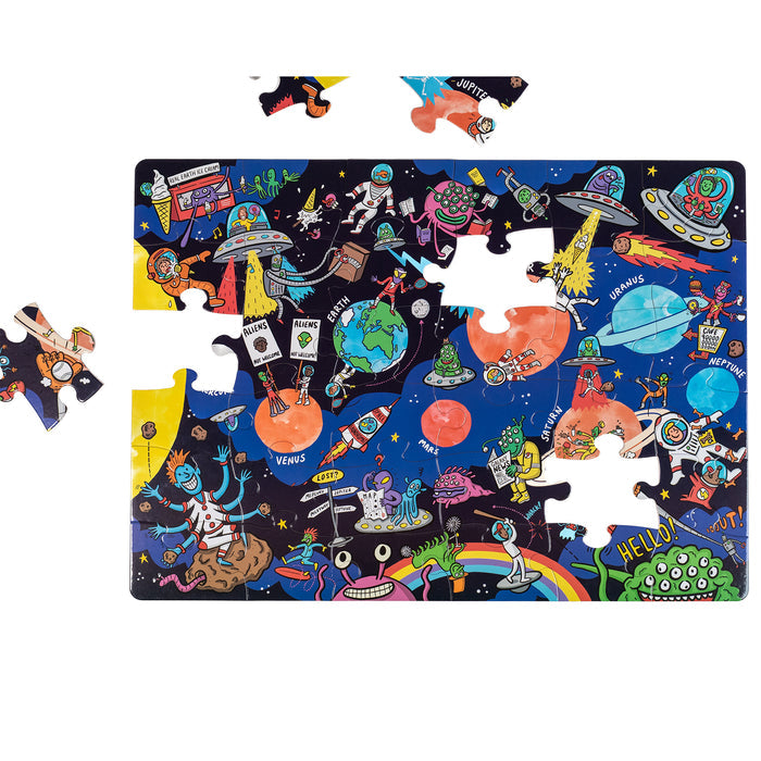 The Nolja Space 36pc Jigsaw Puzzle by Nolja features cartoon aliens, rockets, planets, astronauts, and UFOs. A few pieces are missing, creating visible gaps near the top and left edges of this colorful puzzle.