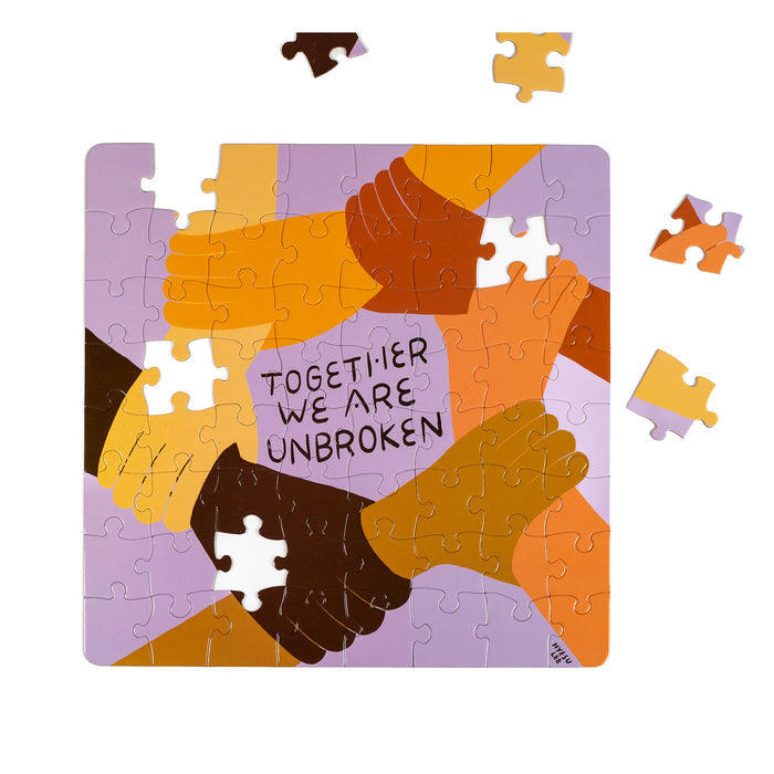 The Nolja Unbroken 64pc Jigsaw Puzzle by Nolja features interlocking hands of diverse skin tones and the message "TOGETHER WE ARE UNBROKEN," with four pieces outside the main artwork, encouraging interactive play.