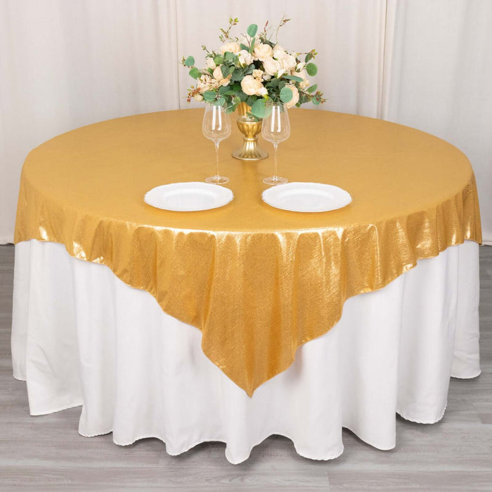 Gold tablecloth with elegant floral centerpiece and dinnerware on a round table.
