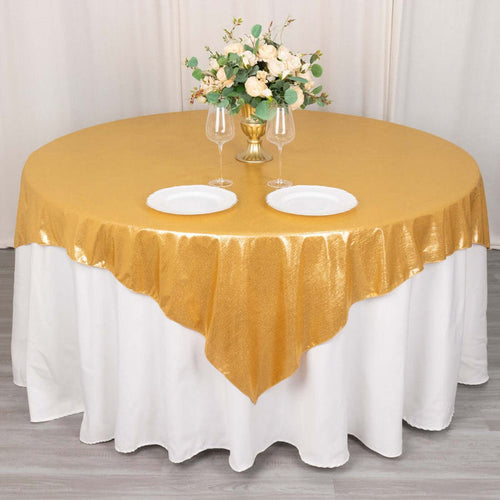 Gold tablecloth with elegant floral centerpiece and dinnerware on a round table.