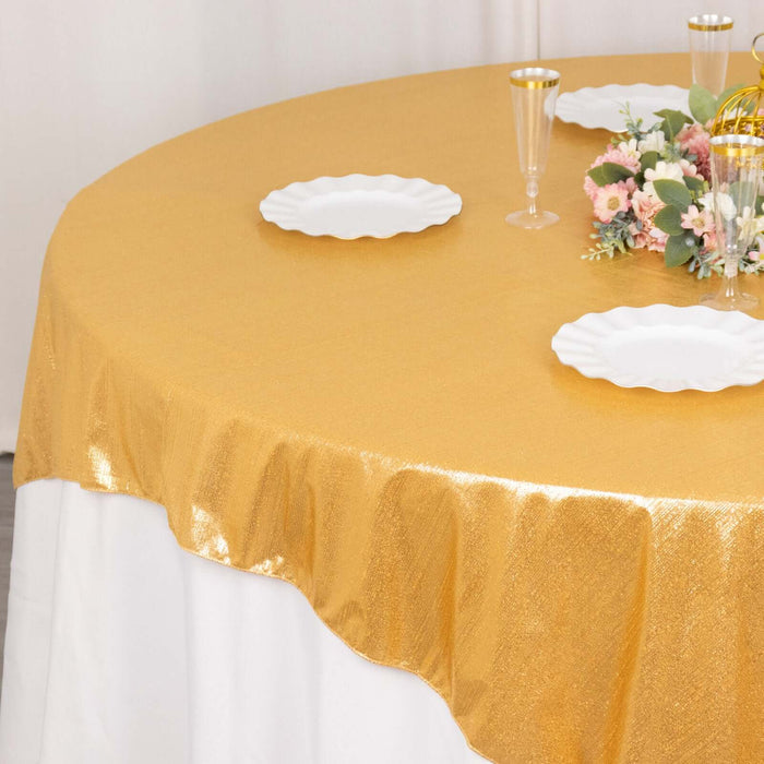 Gold sequin tablecloth draped over a round table with white plates and floral arrangement.