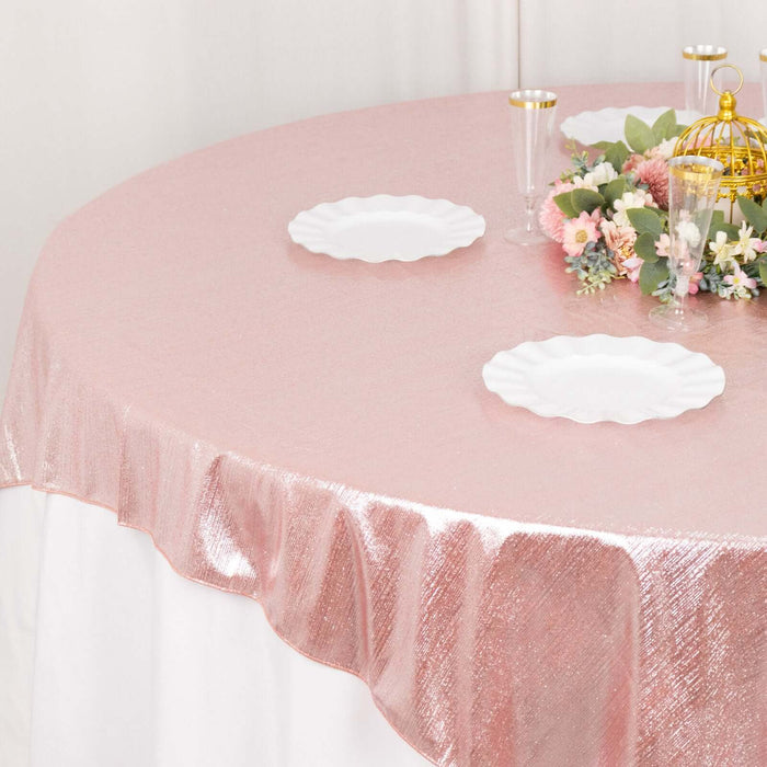 Pink shimmer tablecloth on a round table with white plates and floral centerpiece.