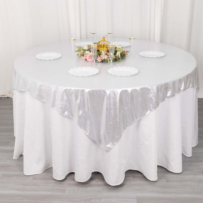 Round table set with a silver tablecloth and white plates, adorned with floral centerpiece.