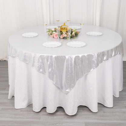 Round table set with a silver tablecloth and white plates, adorned with floral centerpiece.