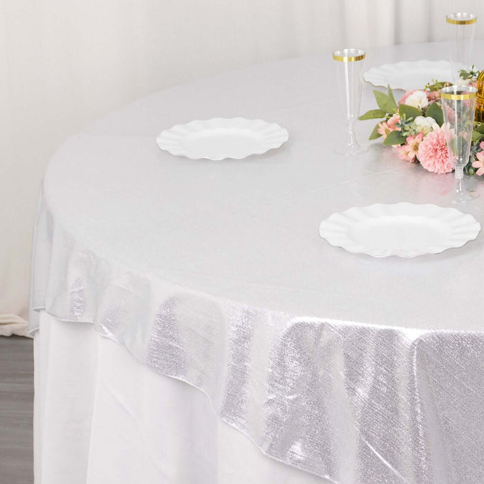Silver tablecloth draped over a round table with white plates and floral centerpiece.