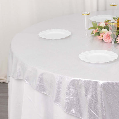 Silver tablecloth draped over a round table with white plates and floral centerpiece.