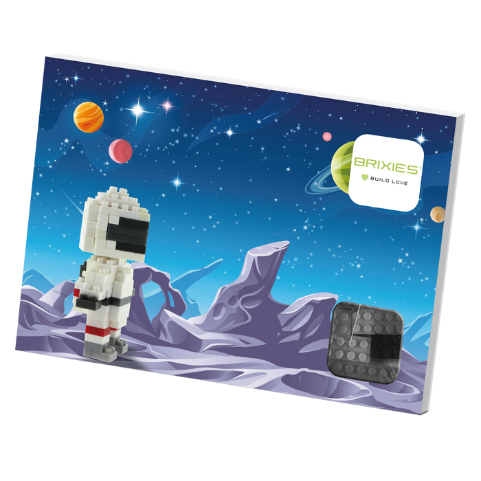 A Brixies Postcard Astronaut micro-brick figure stands on a purple rocky landscape beneath stars and colorful planets in a blue space sky. The white Brixies logo appears in the top right corner.