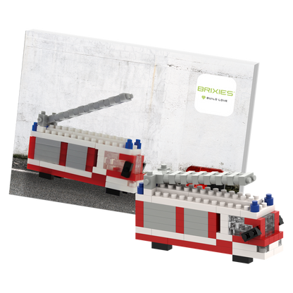 The Brixies Postcard Fire Truck is a LEGO-style mini build kit with a gray ladder, displayed in front of its instruction booklet—a fun, mailable postcard for builders and collectors.