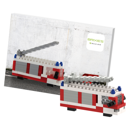 The Brixies Postcard Fire Truck is a LEGO-style mini build kit with a gray ladder, displayed in front of its instruction booklet—a fun, mailable postcard for builders and collectors.