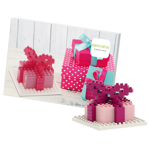 The Brixies Postcard Gift features a small pink and red 3D gift box built from micro bricks, displayed in front of a postcard showing several wrapped presents, including a pink polka-dotted box with a blue ribbon.