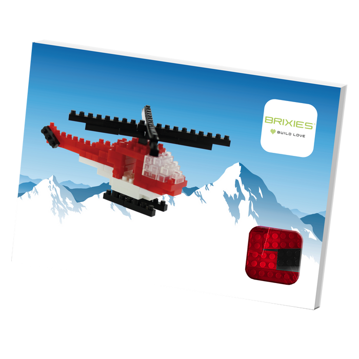 A box featuring a red and white Postcard Helicopter built from micro bricks flying before snowy mountains, with the Brixies logo and BUILD LOVE tagline in the top right corner, and a mini build kit shown at the bottom right.