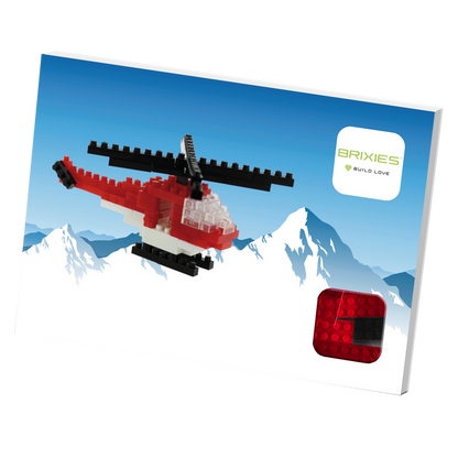 A box featuring a red and white Postcard Helicopter built from micro bricks flying before snowy mountains, with the Brixies logo and BUILD LOVE tagline in the top right corner, and a mini build kit shown at the bottom right.