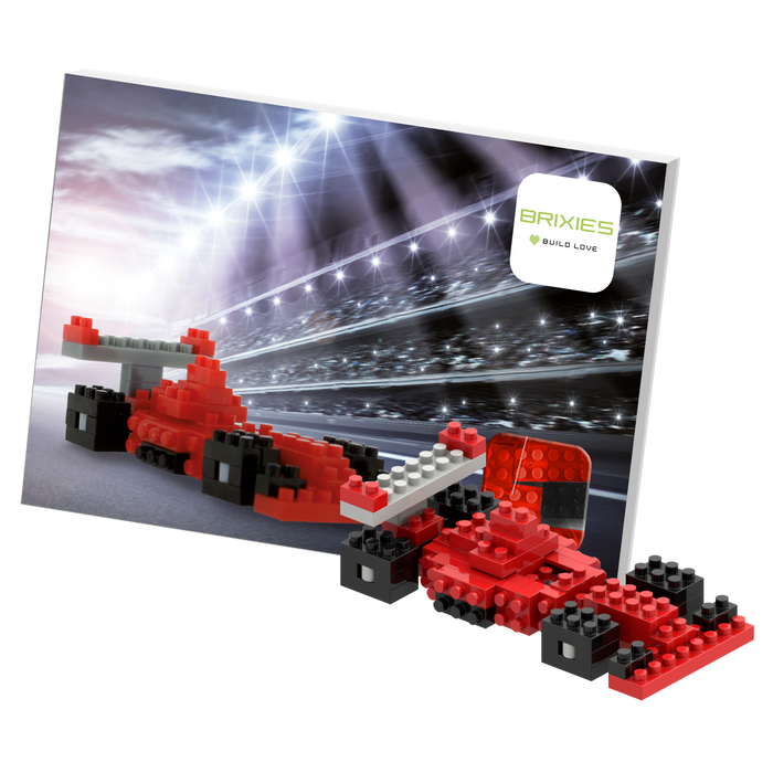 The Brixies Postcard Racing Car is a micro brick model in red and black, showcased with a racing-themed backdrop, track lights, and Brixies logo—a perfect mini build kit for fans of race car postcards.