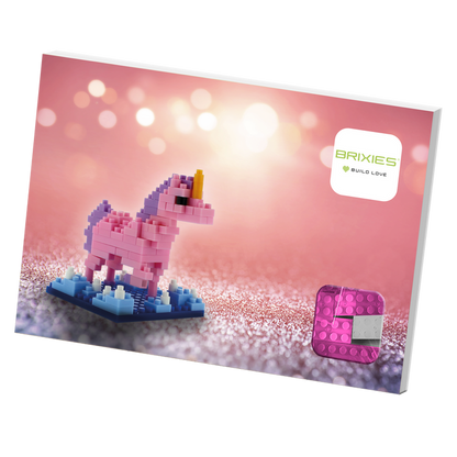 The Brixies Postcard Unicorn features a pink and purple unicorn micro brick kit, set against a sparkling pink background with the Brixies logo and a pink building block in the lower right corner.