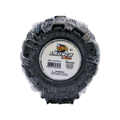 A round black Rollin' Launch 'N Race toy tire, wrapped in plastic and labeled for ages 3+. The center has a barcode and a choking hazard warning for under 3 years. Perfect for use with your favorite die-cast vehicle!.