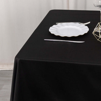 Black tablecloth with white plate and cutlery set for dining.
