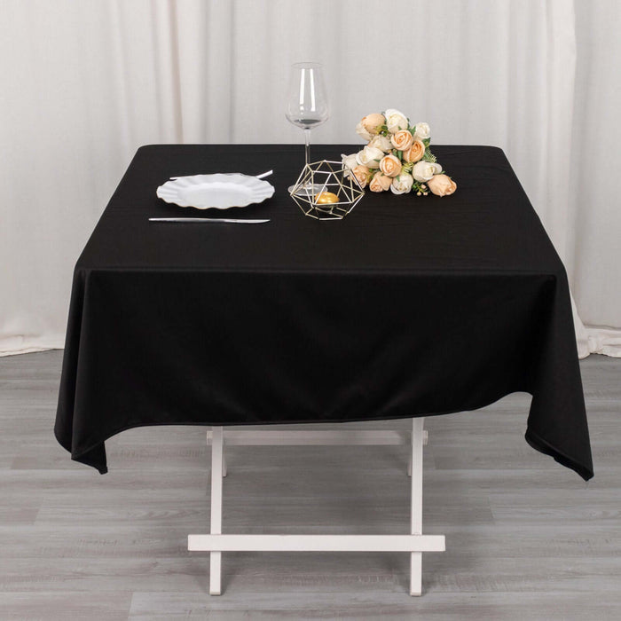 Black tablecloth on a dining table set with a glass and decorative flowers.