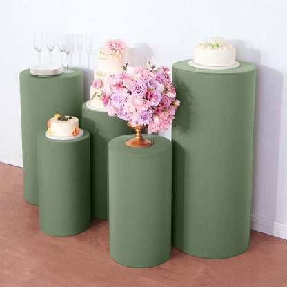 Green display pedestals with cakes and floral arrangements on a neutral background.