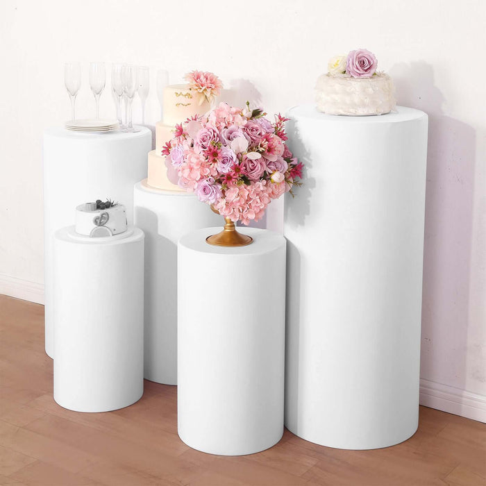 White pedestals displaying floral arrangements and cakes in a studio setting.
