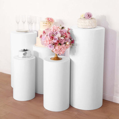 White pedestals displaying floral arrangements and cakes in a studio setting.