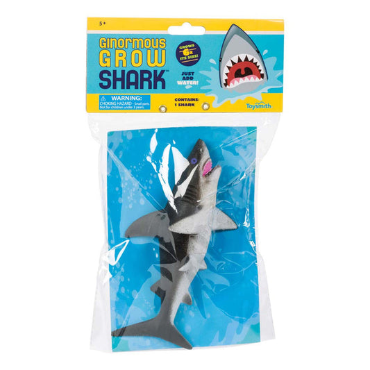 The Toysmith Ginormous Grow Shark by Toysmith displays a gray shark figure in a clear bag with blue backing, featuring an illustrated shark head and text showing it expands when placed in water.