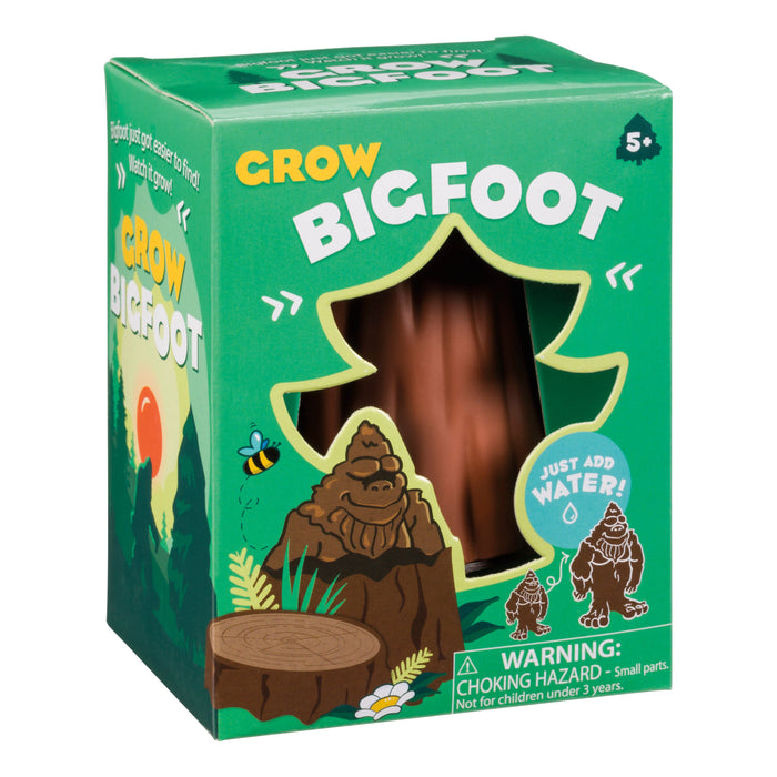 The Toysmith Grow Bigfoot by Toysmith comes in a green box with a tree-shaped window showing the brown toy inside. The packaging features cartoon images of Bigfoot, a bee, a tree stump, and includes a choking hazard warning.